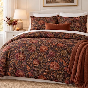 Puede incluir: Un juego de cama que incluye una funda nórdica y fundas de almohada de color marrón oscuro con un denso estampado floral de crisantemos naranjas, rojos y dorados. Un cojín rectangular de color óxido y una manta texturizada de color óxido.