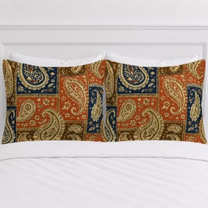 May include: Two rectangular pillow shams featuring a patchwork design of paisley patterns in shades of burnt orange, navy blue, and cream. The fabric displays a repeating motif of teardrop-shaped paisley elements and small floral accents.