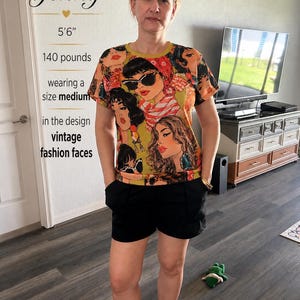 May include: A short-sleeved crew neck t-shirt featuring a repeating graphic print of stylized faces with sunglasses and headscarves in shades of olive green, orange, and black, paired with solid black shorts.