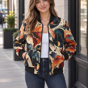 May include: A bomber jacket featuring a multi-coloured abstract print with shades of orange, deep blue, and cream. The jacket has a black ribbed collar, black ribbed cuffs, and a black ribbed hem, with a full-length front zip closure.