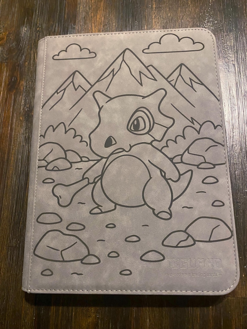 May include: Grey card binder featuring a Cubone illustration with mountains and clouds. The Cubone is holding a bone. The binder has the text "Feel Guard" at the bottom.