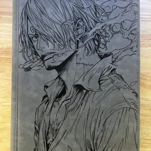 May include: A rectangular gray leather-like binder featuring a laser-engraved illustration of a male anime character with messy hair, a cigarette in his mouth, and a visible scar on his neck, wearing a collared shirt with an open neckline.