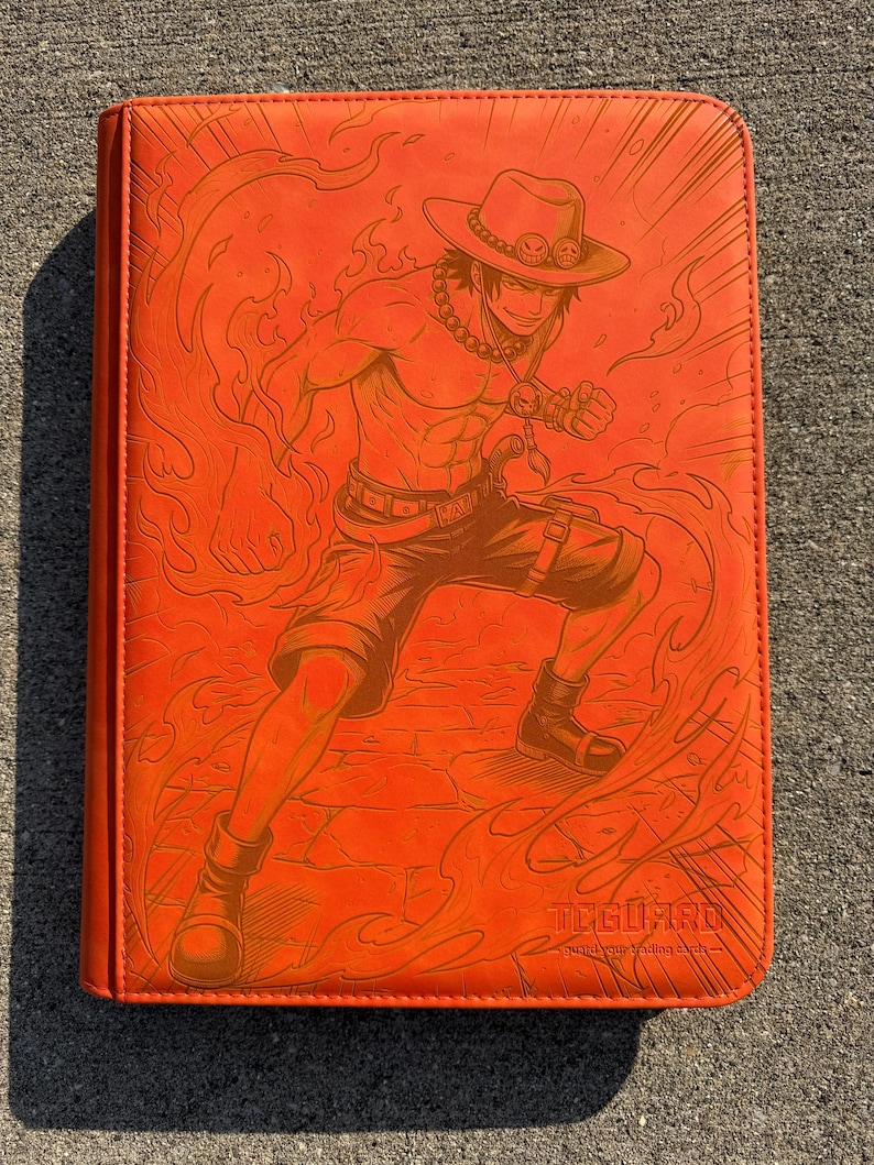 May include: A bright orange trading card binder featuring an embossed illustration of a character wearing a hat and shorts surrounded by flames. The cover includes the text TCGUARD and the phrase guard your trading cards in the bottom right corner.