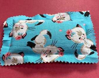 May include: A blue fabric cat-themed heating pad with white cats and pink flowers. The pad has a scalloped edge.