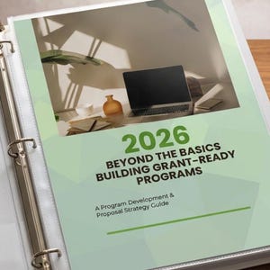 May include: A white binder with a light green cover featuring the text "2026 BEYOND THE BASICS BUILDING GRANT-READY PROGRAMS". The cover also includes a laptop, a small orange vase, and a plant.