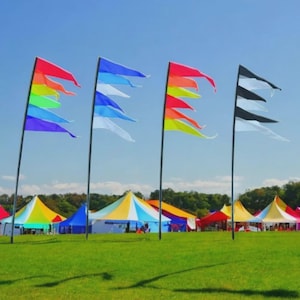 May include: A vibrant outdoor scene featuring colourful flags fluttering in the breeze. The flags display rainbow, blue, red, and black and white patterns. In the background, there are several tents of various colours, set up on a green grassy field under a clear blue sky.