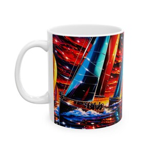 Peut inclure: Un mug en céramique blanche orné d'une illustration vive et colorée de voiliers sur l'eau. Le motif représente plusieurs bateaux aux voiles bleues, rouges et jaunes sous un ciel étoilé rouge et orange dramatique, avec des reflets sur l'eau.