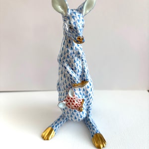 May include: A porcelain kangaroo figurine with a blue and white pattern. The kangaroo has gold accents on its paws, nose, and ears. A baby kangaroo is in the pouch. The figurine is standing upright.