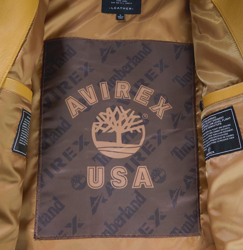 May include: Mustard yellow leather jacket interior with a brown lining. The lining features the Avirex and Timberland logos, along with the text "USA". The jacket has a classic design.