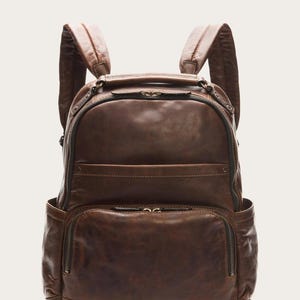 May include: A brown leather backpack with multiple zippered compartments and adjustable shoulder straps. The bag has a top handle and side pockets. The leather has a distressed appearance.