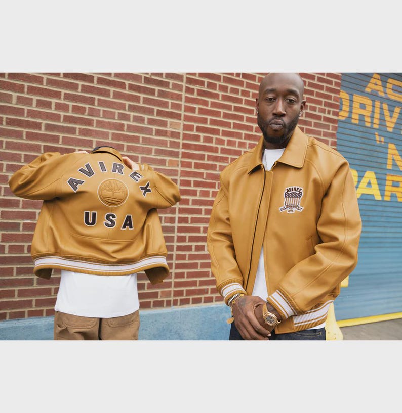 May include: Mustard-colored leather jacket with the text "AVIREX USA" on the back and a patch on the front. The jacket has a collared neckline, ribbed cuffs, and a white and tan striped hem.