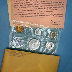 Könnte beinhalten: Ein 1962er US-Proof-Münzensatz in einem transparenten Umschlag, mit einem braunen Papierumschlag und einem beigefarbenen Papiereinsatz. Der Einsatz enthält Text zur Münzpflege. Der Satz enthält einen Penny, Nickel, Dime, Quarter und Half-Dollar.