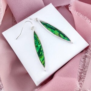 May include: A pair of silver dangle earrings with green abalone shell inlays. The earrings are oval shaped and have a silver hook closure.