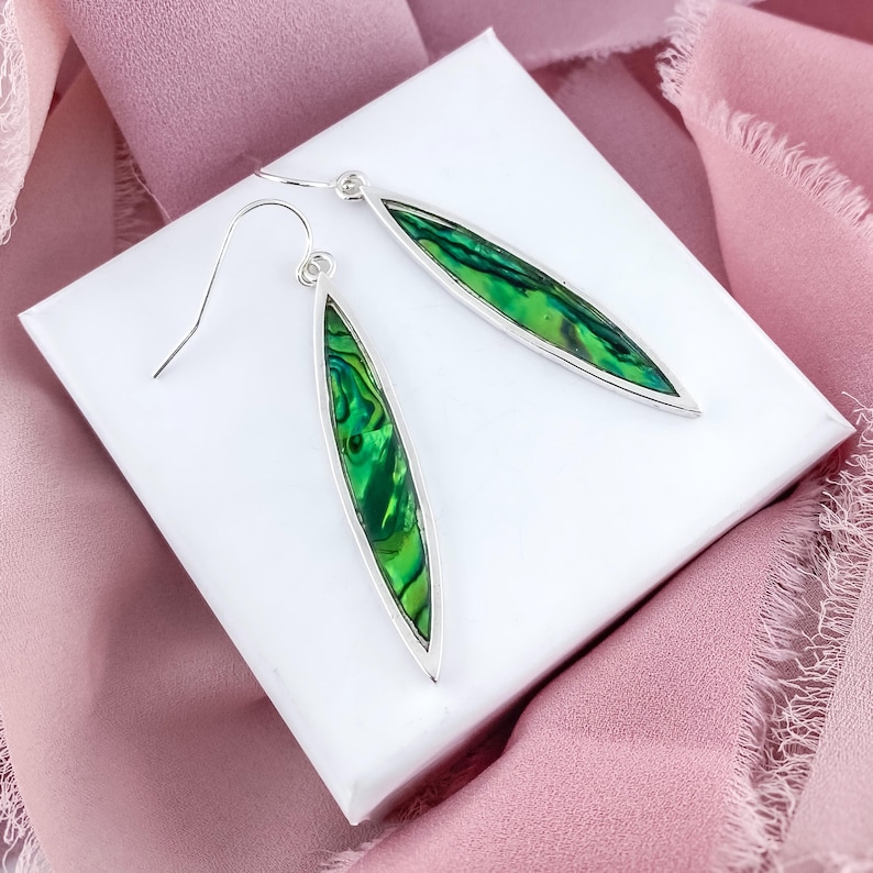 May include: A pair of silver dangle earrings with green abalone shell inlays. The earrings are oval shaped and have a silver hook closure.