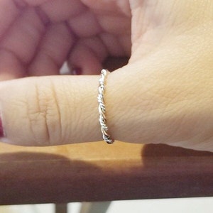 May include: A silver twisted band ring worn on a finger.