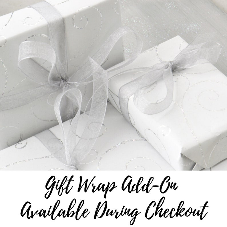 May include: White gift boxes with silver ribbon and a silver swirl pattern. The text "Gift Wrap Add-On Available During Checkout" is displayed below the boxes.