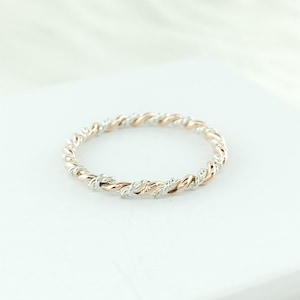 May include: A delicate, twisted ring made of both silver and rose gold. The ring is a simple band with a subtle, elegant design.