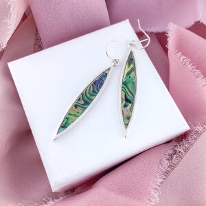 May include: A pair of silver earrings with iridescent abalone shell insets. The earrings are long and oval shaped.