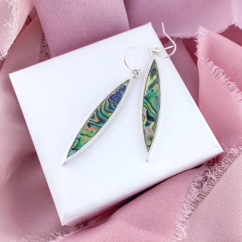 May include: A pair of silver earrings with iridescent abalone shell insets. The earrings are long and oval shaped.