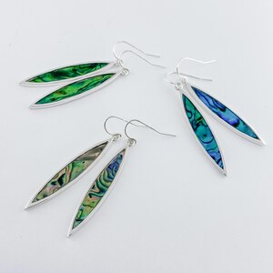 May include: A pair of silver earrings with abalone shell inlays. The earrings are oval shaped and have a green and blue iridescent sheen.