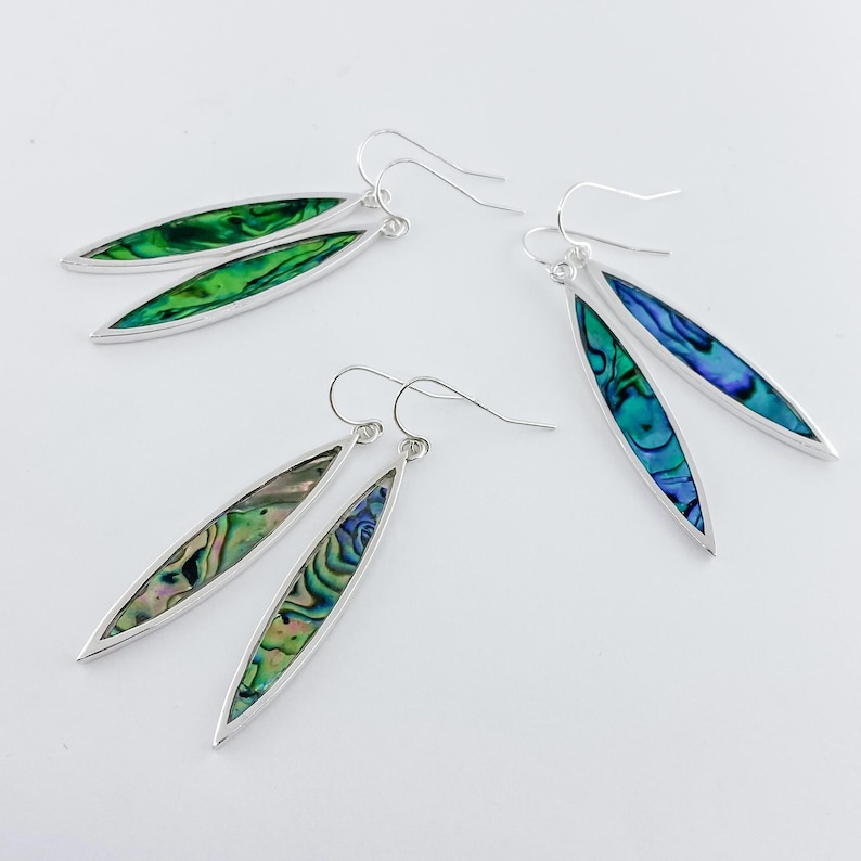 May include: A pair of silver earrings with abalone shell inlays. The earrings are oval shaped and have a green and blue iridescent sheen.