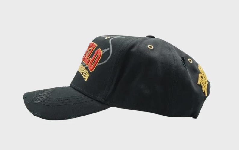 May include: Black baseball cap with the word "FIELD" in red and gold embroidery. The word "CHAMPION" is embroidered in gold. The cap has a curved brim and a distressed look.