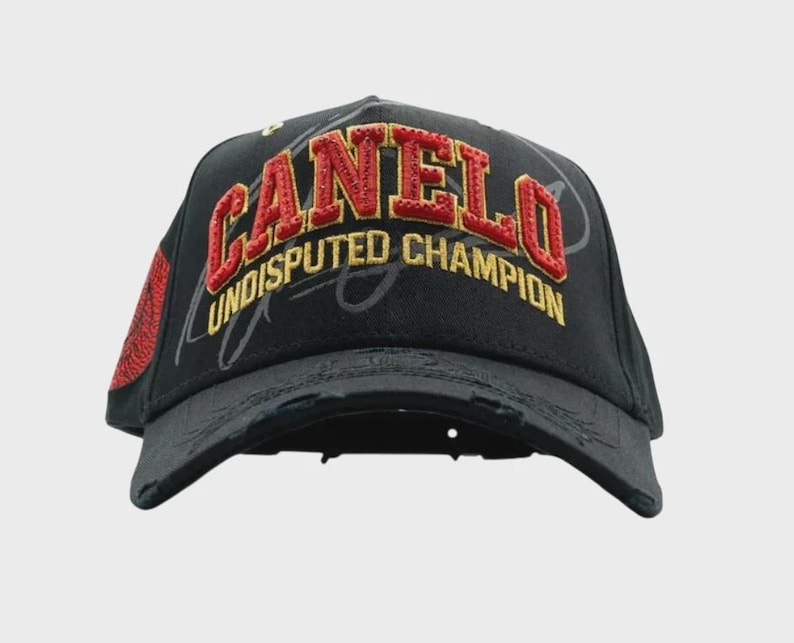 May include: Black baseball cap with the word "CANELO" in red and gold embroidery. The text "UNDISPUTED CHAMPION" is embroidered in gold. The cap has a distressed look and a red patch on the side.