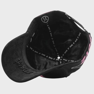 May include: Black baseball cap with a curved brim and adjustable strap. The cap features the word "SADBOY" embroidered on the front and pink text on the side. The interior has a white logo and text.