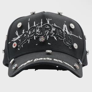 May include: Black baseball cap with the word "Dared" embroidered in white script. The cap is embellished with multiple rhinestones and the text "My Dark Side" on the brim.
