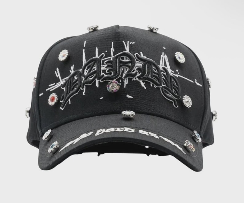 May include: Black baseball cap with the word "Dared" embroidered in white script. The cap is embellished with multiple rhinestones and the text "My Dark Side" on the brim.