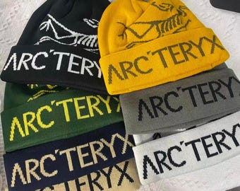Berretto in maglia Arc'teryx con logo dinosauro, ideale per attività all'aperto e streetwear.