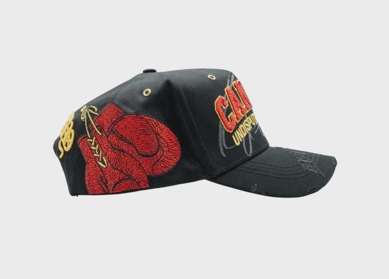 May include: Black baseball cap with embroidered red boxing gloves and gold accents. The cap features the word "CAN" in red and gold embroidery, with "UNDISPUTED" below. A stylish accessory for sports enthusiasts.