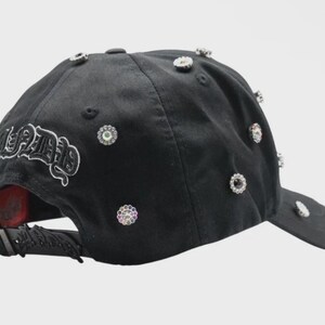 May include: Black baseball cap adorned with multiple sparkling rhinestones and the word "SEETHE" in white script. The cap features a curved brim and an adjustable strap at the back. A stylish accessory.