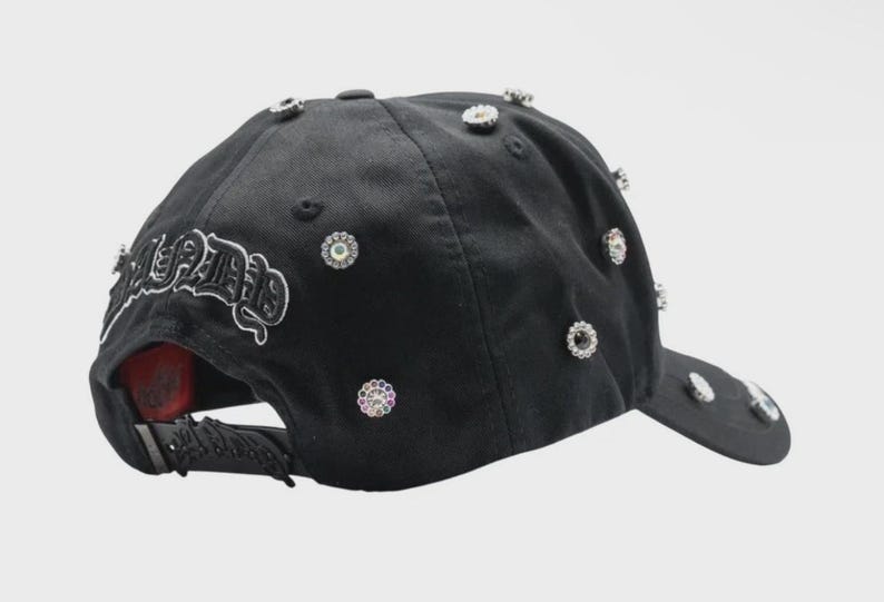 May include: Black baseball cap adorned with multiple sparkling rhinestones and the word "SEETHE" in white script. The cap features a curved brim and an adjustable strap at the back. A stylish accessory.