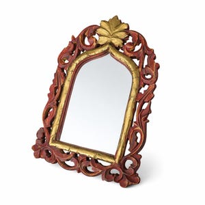 Peut inclure: Miroir décoratif avec un cadre en bois sculpté rouge et doré. Le cadre présente des motifs floraux et volutes complexes. Le miroir a une forme arquée et un accent de feuille d'or en haut. Le miroir est autoportant.