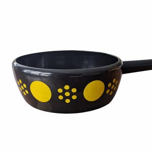 Peut inclure: Un caquelon noir avec une poignée et des cercles et points décoratifs jaunes. Le caquelon est conçu pour la cuisson et le service de fromage ou de chocolat fondu. La poignée est fixée sur le côté du caquelon.