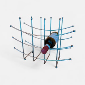 May include: A blue metal wine rack holding a wine bottle. The rack has a grid-like design with curved horizontal bars and vertical supports. The wine bottle has a red cap and a label.