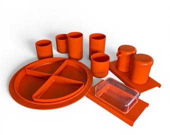 May include: An orange plastic camping set featuring plates, cups, and containers. The set includes divided plates, various sized cups, and lidded containers. The items are arranged on a white surface.