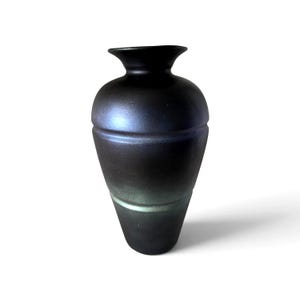May include: A matte black vase with a tapered base and a wide, flared rim. The surface features a subtle iridescent sheen that shifts from deep black to hints of dark blue and green, with a horizontal band encircling the midsection of the body.
