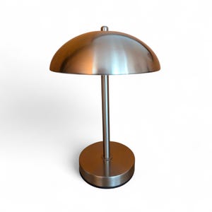 May include: A brushed nickel table lamp with a dome-shaped shade. The lamp has a circular base and a slender stem. The shade is a half-sphere shape. The lamp is designed for indoor use and provides ambient lighting.