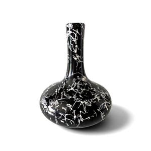 May include: A black vase with a narrow neck and a rounded base, featuring a white marbled or splattered paint pattern across the entire surface. The object has a smooth, glossy finish and a distinct bulbous shape that tapers into a slender opening.