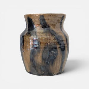 May include: A ceramic vase with a wide, rounded body and a flared rim. The surface features a mottled glaze with vertical streaks of dark charcoal and black layered over a warm, earthy tan and brown base, creating a textured, multi-tonal appearance.