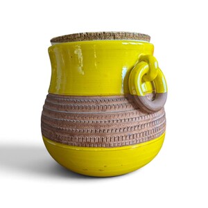 Peut inclure: Un pot en céramique jaune vif avec un couvercle en liège. Le pot présente une large bande brune texturée au centre avec un motif géométrique répétitif. Une épaisse poignée en anneau en céramique jaune est fixée sur le côté supérieur.
