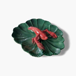 May include: A ceramic serving dish with a vibrant red lobster on a large, green leaf-shaped platter. The lobster has detailed claws and a textured body. The dish is likely used for serving seafood or as a decorative piece.
