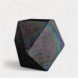 May include: A faceted, geometric vase with a dark, iridescent finish. The vase has a cracked, textured surface that reflects a spectrum of colors, including purple, green, and blue. The vase is a decorative item.