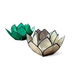 Peut inclure: Deux bougeoirs en forme de fleur de lotus. L'un est vert vif, l'autre beige nacré. Les deux ont des contours noirs et sont conçus pour contenir des bougies, ajoutant une touche de décoration inspirée de la nature.