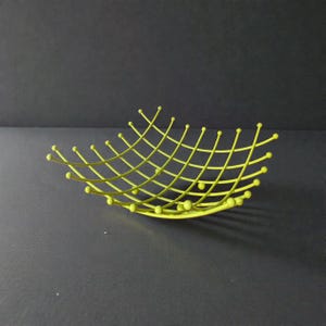 Peut inclure: Un bol en fil métallique vert citron doté d'une structure en grille avec des tiges métalliques incurvées. Chaque intersection et extrémité de la structure en fil est terminée par une petite perle arrondie, créant un design ajouré symétrique.
