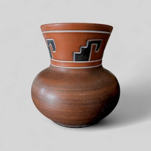 Peut inclure: Vase en céramique marron avec un corps arrondi et un col évasé. Le col présente une bande orange-rougeâtre avec des motifs géométriques noirs et blancs. Le vase a une esthétique rustique et terreuse.