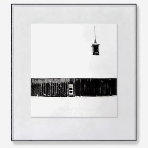 Peut inclure: Tirage encadré en noir et blanc d'un bâtiment dans un paysage enneigé. Le bâtiment présente une façade sombre et texturée avec une petite fenêtre. Un élément décoratif surmonte le bâtiment. L'impression est encadrée dans un passe-partout blanc et un cadre noir.