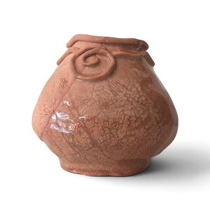 May include: A small, bulbous terracotta-coloured ceramic vase with a wide opening and a narrow base. The surface features a distinct crackle glaze texture and a raised, hand-applied spiral decorative element encircling the upper neck area.